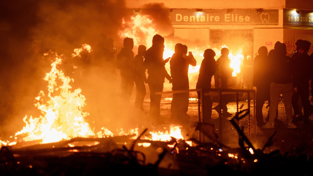 Burning cars, barricades, and fires in streets of Paris at night during rioting by adherents of the red-green alliance; October 17, 2026.