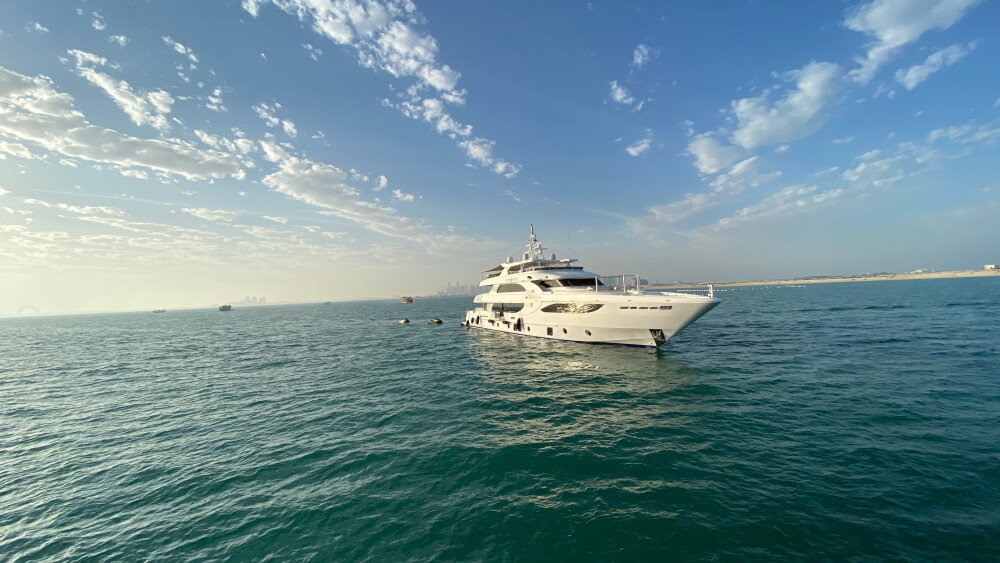 A yacht sails the waters of the Persian Gulf in May 2025, with the distant skyline of Doha, Qatar, faintly visible.