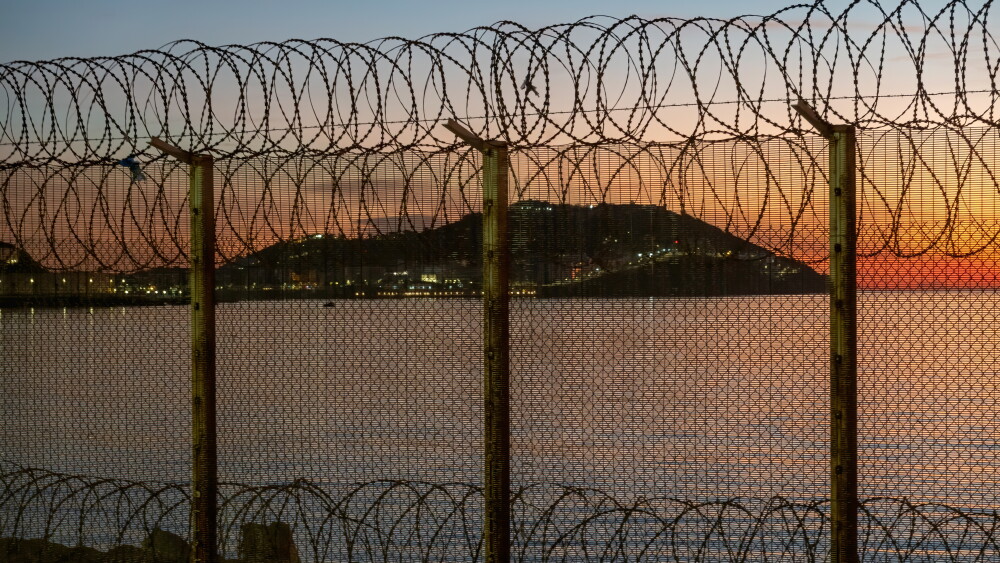 For decades, Morocco has understood that migration can serve purposes extending far beyond humanitarian need. Properly controlled – or deliberately left uncontrolled – migration becomes a remarkably effective instrument of statecraft. Image: Ceuta, a Spanish city in North Africa, seen from Morocco behind a thorn wire fence located on the Moroccan border, against a sunset over the sea.
