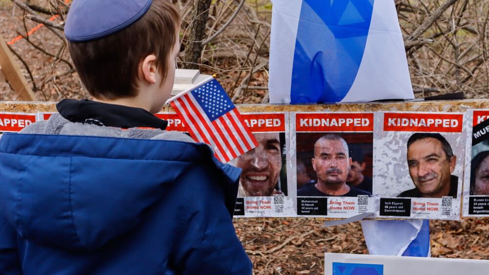 A boy looks at posters of Israeli hostages at the Homer Street memorial in Newton, Mass., during a community gathering on April 7, 2024, to rebuild the display. A Newton resident put up more than 100 posters after the October 7, 2023, attacks. The tribute was vandalized in mid-March 2024, prompting a local hate crime investigation. The attack on the memorial demonstrates how anti-Israel propaganda promoted in public schools and in colleges and universities harms the Jewish diaspora.