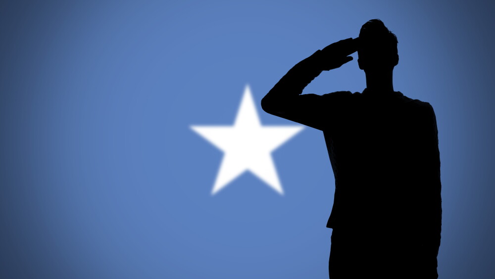 A soldier salutes the flag of Somalia.