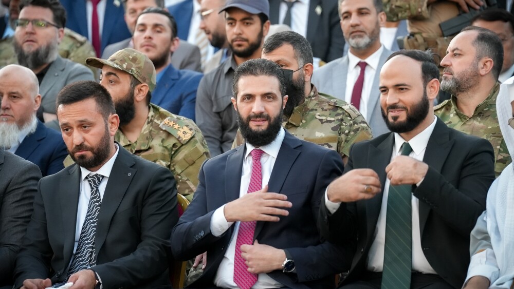Members of the military are among those seated with Syria's interim President Ahmed al-Sharaa (front center) in May 2025.