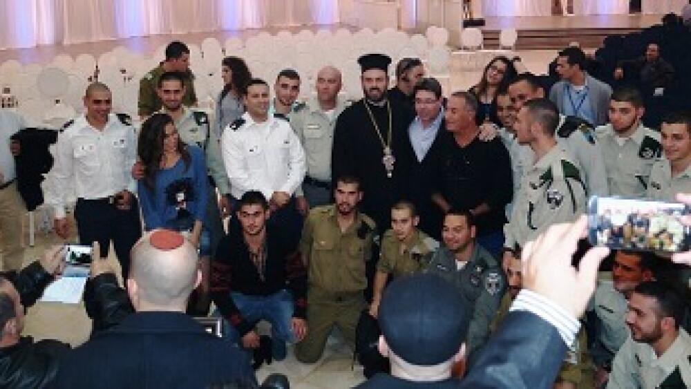 Father Gabriel Naddaf with Deputy Minister Ofir Akunis and Christian IDF soldiers, December 14, 2014. An early leader of Israel’s pro-integration Christian movement, Naddaf encouraged Christian Arabs to embrace an Aramean identity and serve in the Israel Defense Forces despite threats and intimidation against him and his family. (Credit: Wikimedia Commons)