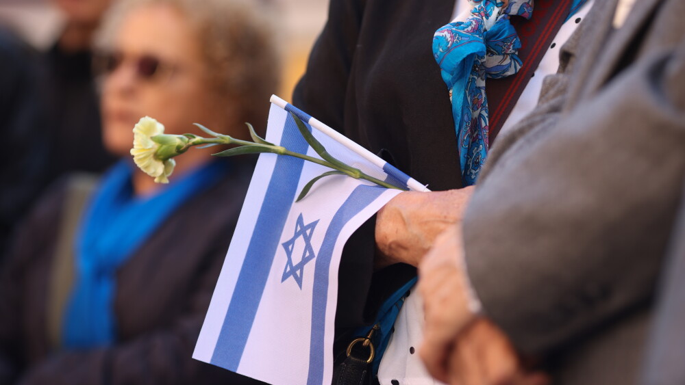 A woman holds the Israeli flag and a flower during a ceremony commemorating the October 7, 2023, attacks.
